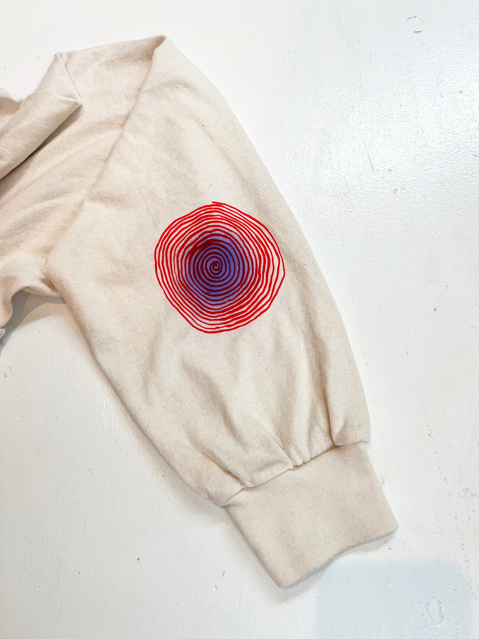 A photo detail of the opposite Maze Tee sleeve featuring a red spiral with a purple airbrushed haze at its center.